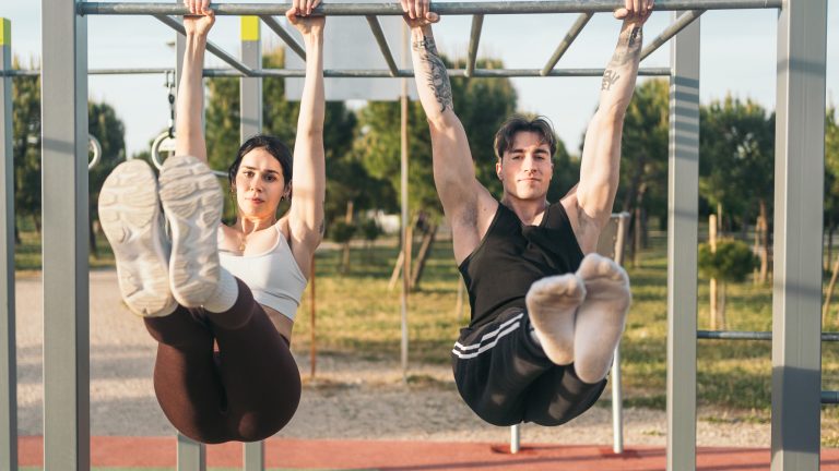 Zwei Personen führen an einer Calisthenics-Station Hanging Leg Raises aus.