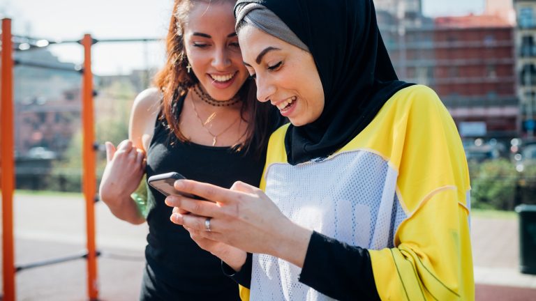 Zwei Personen in Sportbekleidung stehen in einem Calisthenics-Park und blicken gemeinsam in ein Smartphone.