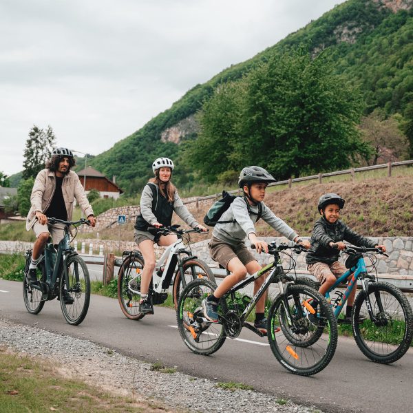 Eine Gruppe Radfahrender ist mit ihren Trekkingr&auml;dern auf einer Stra&szlig;e unterwegs. Im Hintergrund ist ein Berg zu sehen.
