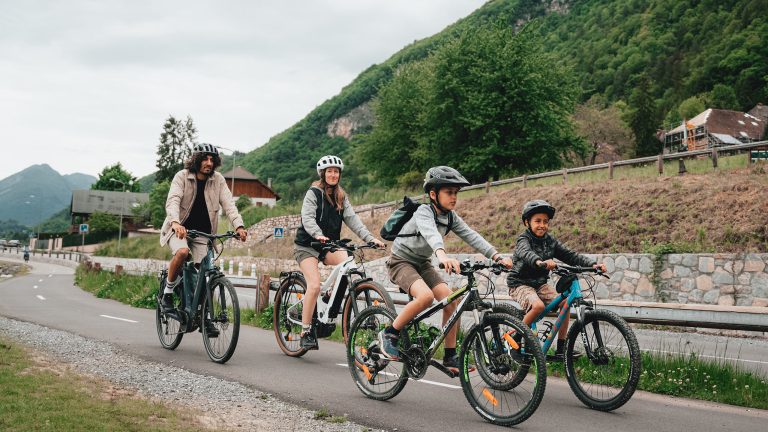 Eine Gruppe Radfahrender ist mit ihren Trekkingr&auml;dern auf einer Stra&szlig;e unterwegs. Im Hintergrund ist ein Berg zu sehen.