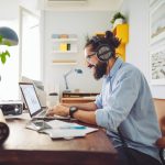 Eine Person sitzt vor einem Laptop an einem Schreibtisch und trägt ein Headset.