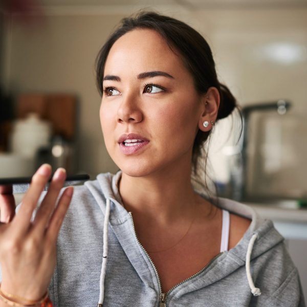 Eine Person in einem grauen Sweatshirt h&auml;lt ihr Smartphone in der Hand, ihr Blick schweift in die Ferne.