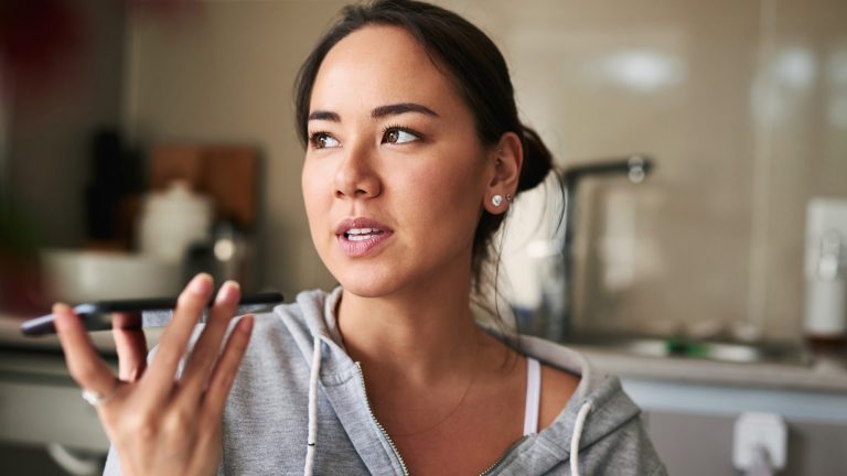 Eine Person in einem grauen Sweatshirt hält ihr Smartphone in der Hand, ihr Blick schweift in die Ferne.