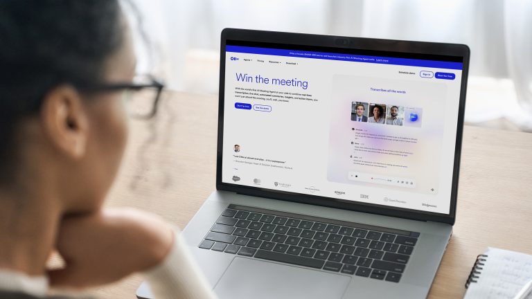 Ein geöffneter Laptop steht auf einem Holzschreibtisch. Auf dem Display ist die Startseite von Otter.ai zu sehen. Eine Person sitzt vor dem Laptop.