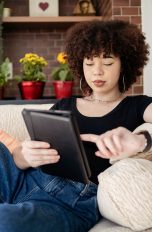Kindle Unlimited, So kündigst du das E-Book-Abo Eine Person liegt auf einem beigen Sofa. In den Händen hält sie ein Tablet.