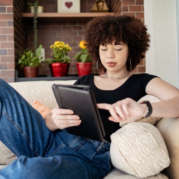 Eine Person liegt auf einem beigen Sofa. In den H&auml;nden h&auml;lt sie ein Tablet.