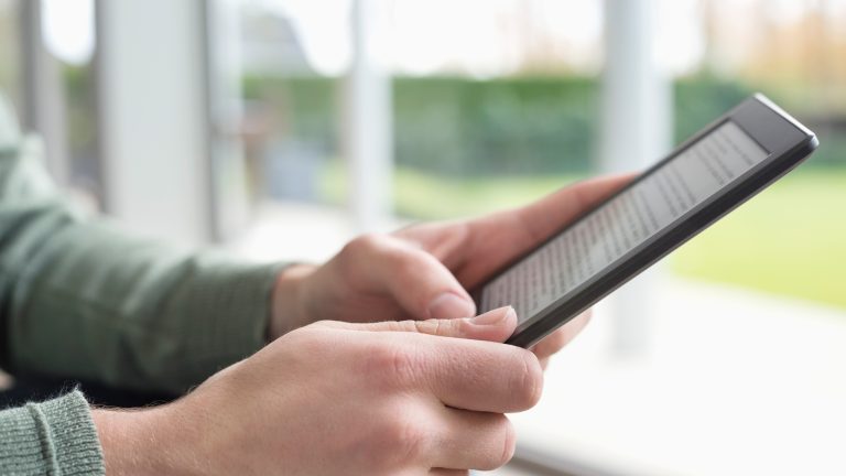 Nahaufnahme zweier Hände, die ein Tablet halten. Das Display zeigt einen Fließtext.