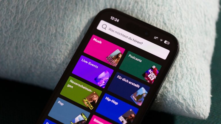 Eine Nahaufnahme eines iPhones, das an einem Kissen lehnt. Darauf ist die Auswahlseite der App Spotify zu sehen.