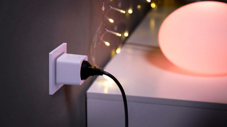 Nahaufnahme einer smarten Steckdose mit einem schwarzen Stecker. Im Hintergrund ist ein Lowboard mit Kugellampe zu erkennen.