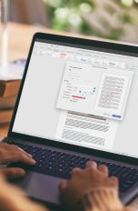 Wasserzeichen in Word einfügen und bearbeiten Eine Person sitzt vor einem Notebook. Auf dem Display ist ein geöffnetes Word-Dokument zu sehen; darüber liegt das Fenster zur Einrichtung eines Wasserzeichens.