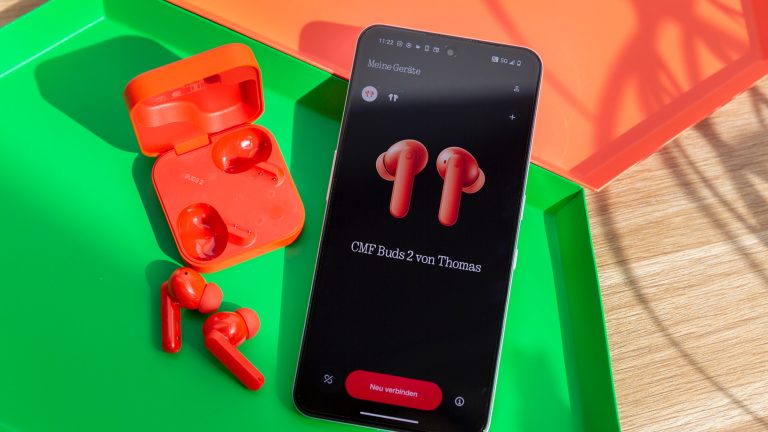 Die CMF Buds 2 in Orange liegen neben einem CMF Phone 2 Pro, auf dessen Display die Kopfh&ouml;rer zu sehen sind.