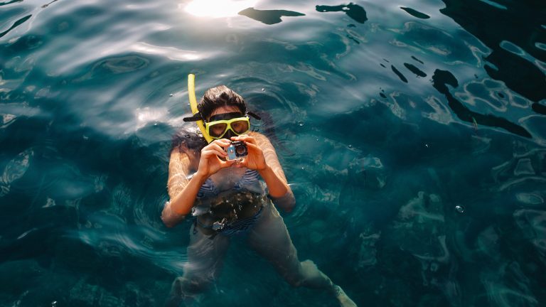 Eine Person treibt mit Taucherbrille und Schnorchel im Wasser. In den Händen hält sie eine kompakte Actionkamera.