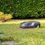 Ein M&auml;hroboter f&auml;hrt &uuml;ber eine gr&uuml;ne Wiese. Im Hintergrund ist eine gr&uuml;ne Hecke zu sehen.