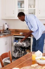 Alt-Text: Eine Person räumt nach dem Frühstück Geschirr in eine Spülmaschine.