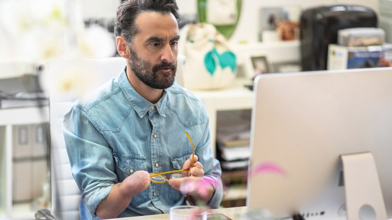 Eine Person mit einer eingeschränkten Arm- und Handfunktion auf der rechten Seite sitzt vor einem Computerdisplay.