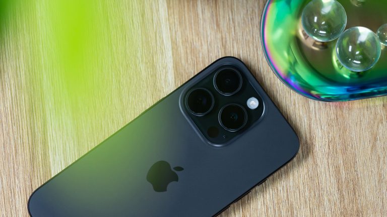 Blick auf ein iPhone 15 Pro, das mit der Rückseite nach oben auf einer Holzoberfläche liegt.