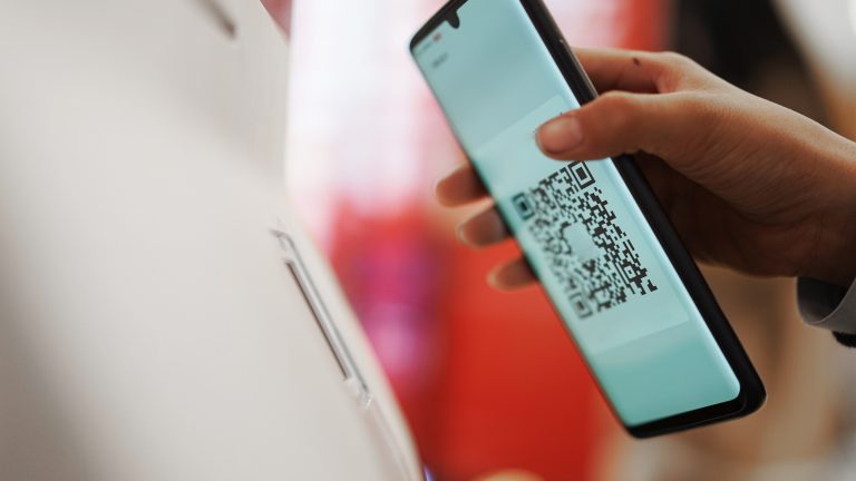 Eine Person hält einen QR-Code auf einem Smartphone an einen QR-Scanner an einem Terminal.