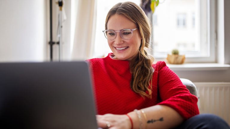Eine Person sitzt auf einem Sofa und schaut in einen Laptop.