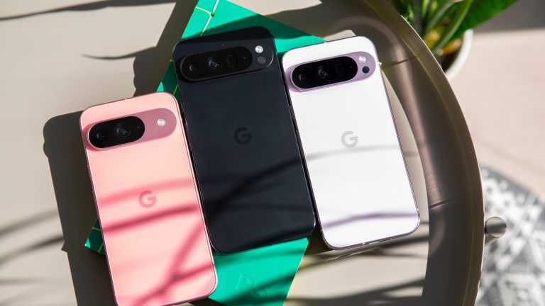 Ein Google Pixel 9 in Pink, ein Pixel 9 Pro und ein Pixel 9 Pro XL liegen nebeneinander auf einem grünen Notizbuch.