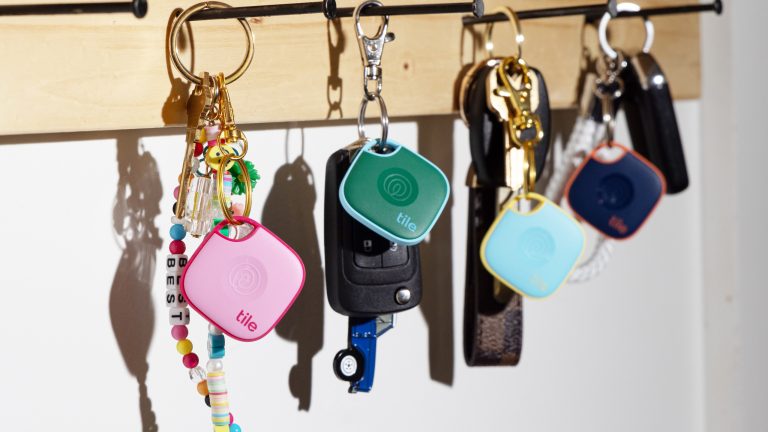 Mehrere Schlüssel mit unterschiedlichfarbigen Tile-Trackern hängen an einzelnen Nägeln an einem Schlüsselbrett.