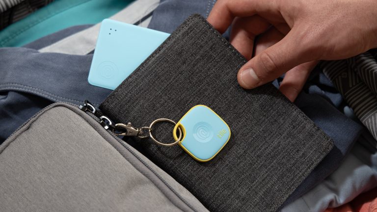 Eine Person hält einen Geldbeutel in der Hand aus dem ein Tile-Card-Tracker herausschaut. Obenauf hängt ein Tile-Tracker an einem Schlüsselkarabiner.