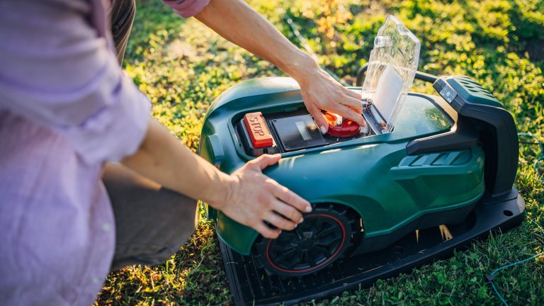 Eine Person prüft einen Mähroboter, dessen Gehäuse geöffnet ist, auf Funktionstüchtigkeit.