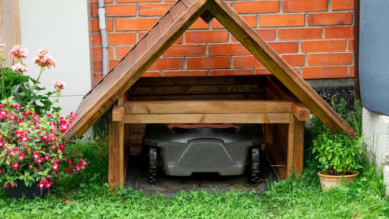 Ein M&auml;hroboter steht in einer selbstgebauten M&auml;hroboter-Garage aus Holz.