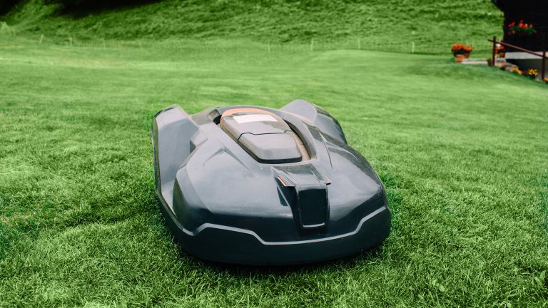 Mähroboter installieren, So bleibt er im grünen Bereich Ein schwarzer Mähroboter fährt über eine große grüne Wiese.
