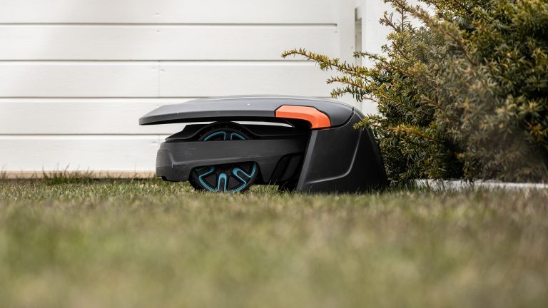 Mähroboter installieren, So bleibt er im grünen Bereich Ein Mähroboter mäht den Rasen vor einem weißen Hochbeet.