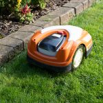 Ein M&auml;hroboter m&auml;ht das Gras am Steinrand eines Beets.