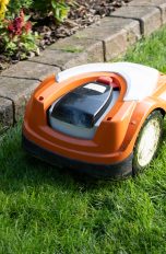 Ein Mähroboter mäht das Gras am Steinrand eines Beets.