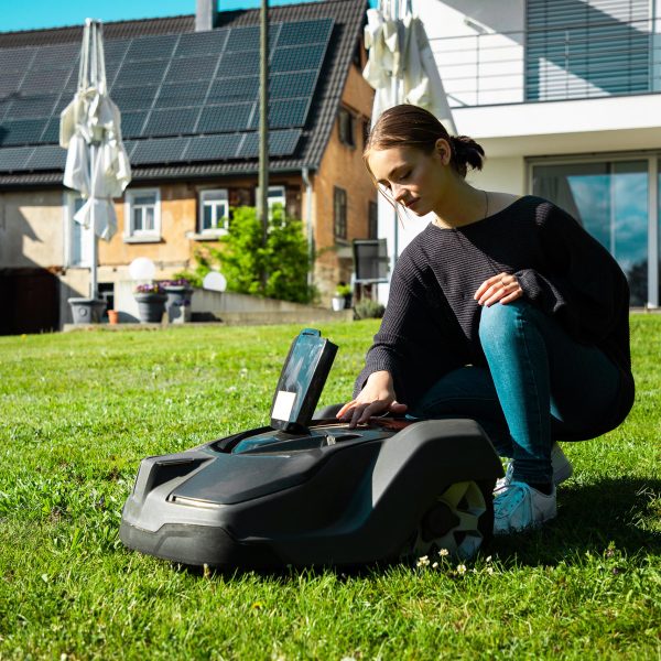 Eine Person kniet hinter einem M&auml;hroboter mit einem ge&ouml;ffneten Geh&auml;use.