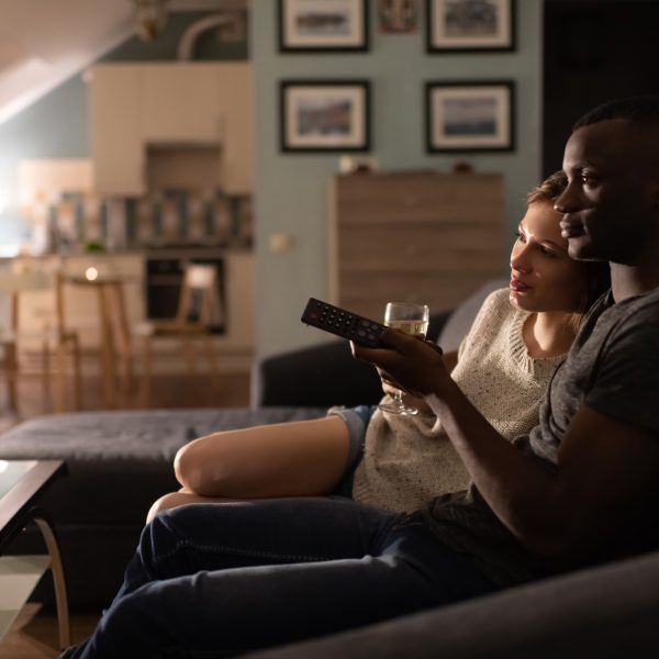 Zwei Personen sitzen auf einem Sofa und schauen TV.