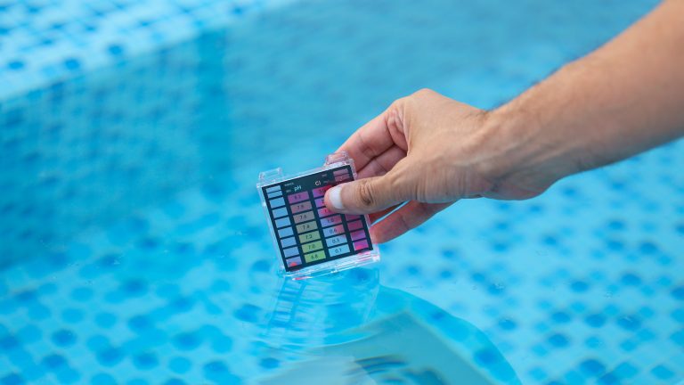 Eine Person hält eine Karte zum Testen des PH-Werts in das Wasser eines Pools.