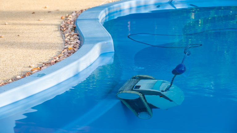 Blick auf die Seite eines Pools in dem ein Poolroboter senkrecht an einer Kante steht.