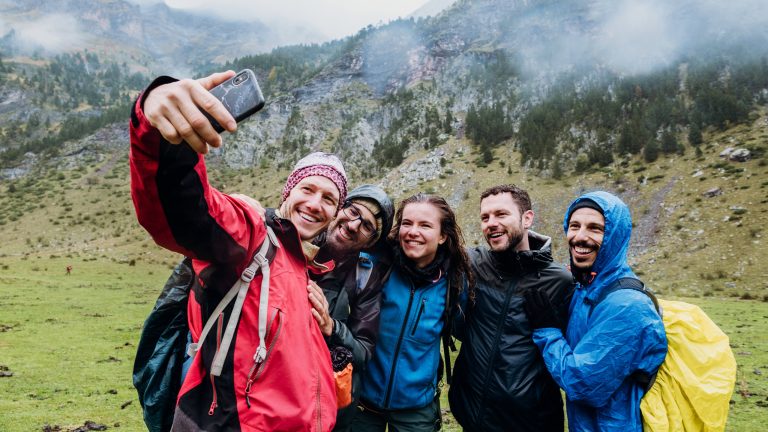 Fünf Personen stehen in einer bergigen Landschaft und machen ein Selfie.