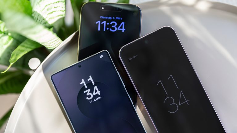 Ein iPhone 16 Pro Max, ein Samsung Galaxy Ultra und ein Google Pixel 9 Pro XL liegen schräg übereinander auf einem runden Metalltisch. Links oben eine Pflanze im Anschnitt.