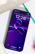 Ein iPhone liegt auf einem weißen Notizbuch. Der Sperrbildschirm ist an.