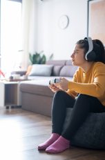 Kopfhörer mit dem Fernseher verbinden, So klappt’s Eine Person auf dem Sofa und schaut konzentriert auf einen Fernseher. Sie trägt Over-Ear-Kopfhörer und hält einen Controller in den Händen.