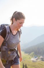 Geschenkidee für Outdoor-Fans, Sechs geniale Technik-Gadgets Seitansicht einer Person in Jeansshorts und mit Wanderrucksack. Im Hintergrund ist alpine Landschaft zu sehen.