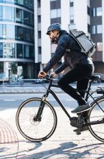 Eine Person auf einem Fahrrad f&auml;hrt durch eine Stadt. Auf ihrem Kopf ist ein schwarzer Helm zu sehen.