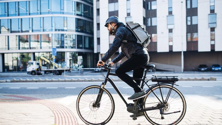 Eine Person auf einem Fahrrad f&auml;hrt durch eine Stadt. Auf ihrem Kopf ist ein schwarzer Helm zu sehen.