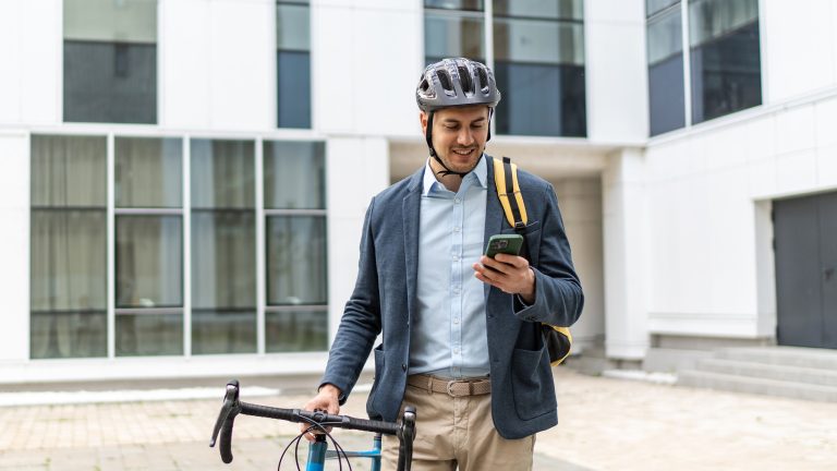 Eine Person mit einem Fahrrad und einem Helm auf dem Kopf schaut auf ihr Smartphone.
