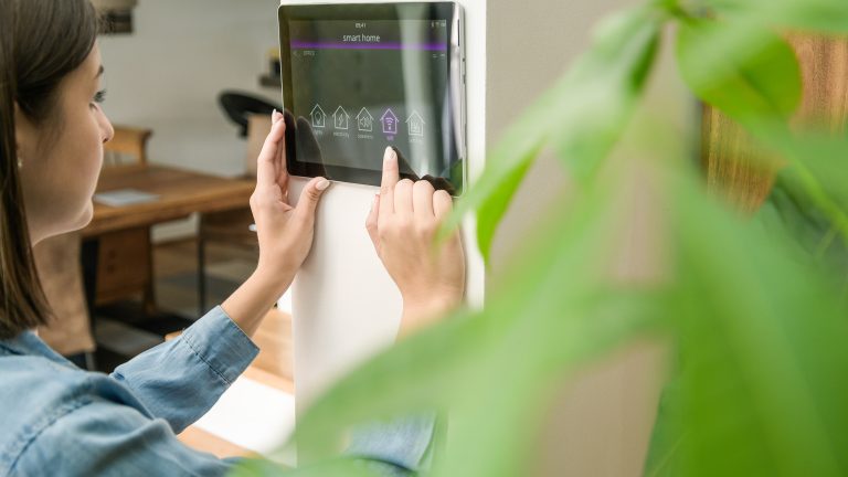 Eine Person steuert Smarthome-Funktionen über ein an der Wand montiertes Tablet.