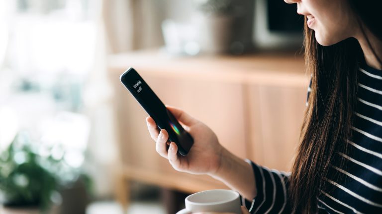 Eine Person hält ein Smartphone in der Hand, auf dem ein Sprachassistent zu sehen ist.