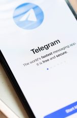 Telefonieren mit Telegram, So gehen Sprach- und Videoanrufe Ein Smartphone auf einem Schreibblock. Links daneben ein Kugelschreiber. Auf dem Screen der Startbildschirm von Telegram.