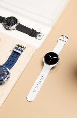 Die Galaxy Watch8, Watch8 Classic und Watch Ultra liegen auf hellen Fl&auml;chen neben einem Stein und einer Pflanze.