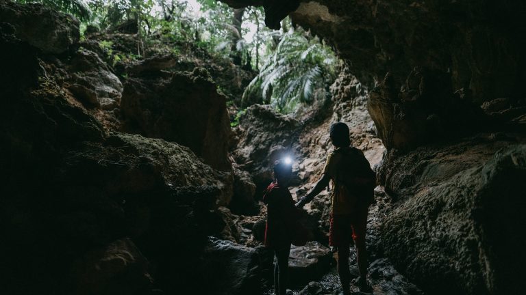 Eine Person und ein Kind stehen in einer Felsgrotte. Das Kind tr&auml;gt eine Stirnlampe am Kopf.