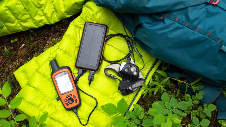 Ein Satellitenkommunikationsger&auml;t liegt auf einem neongr&uuml;nen Schlafsack. Daneben liegt ein dunkelblauer Outdoor-Rucksack.