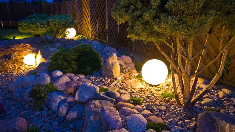 In einem Garten beleuchten mehrere runde Bodenleuchten die Beete.